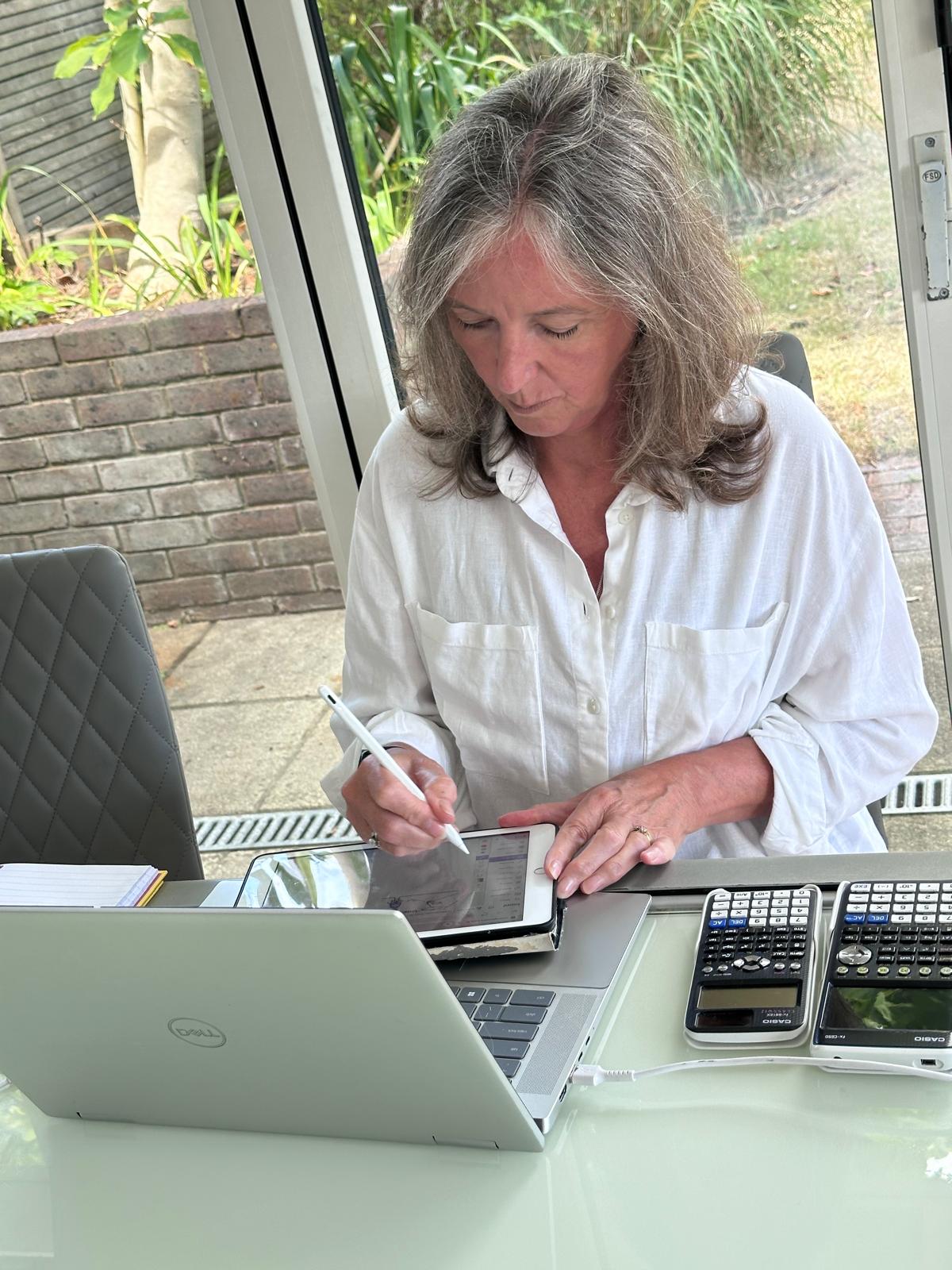 Nikki Nash working at her desk with a laptop, iPad and graphics calculators